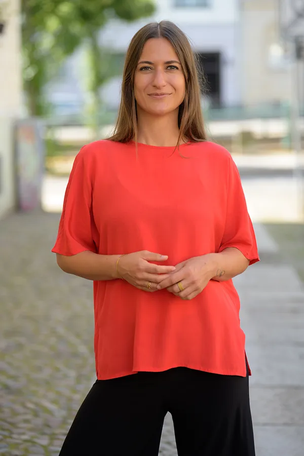 Giulia Barile, DGSv-zertifizierte systemische Supervisorin in Köln und Coach für berufliche Neuorientierung, in einem roten Shirt stehend auf der Straße