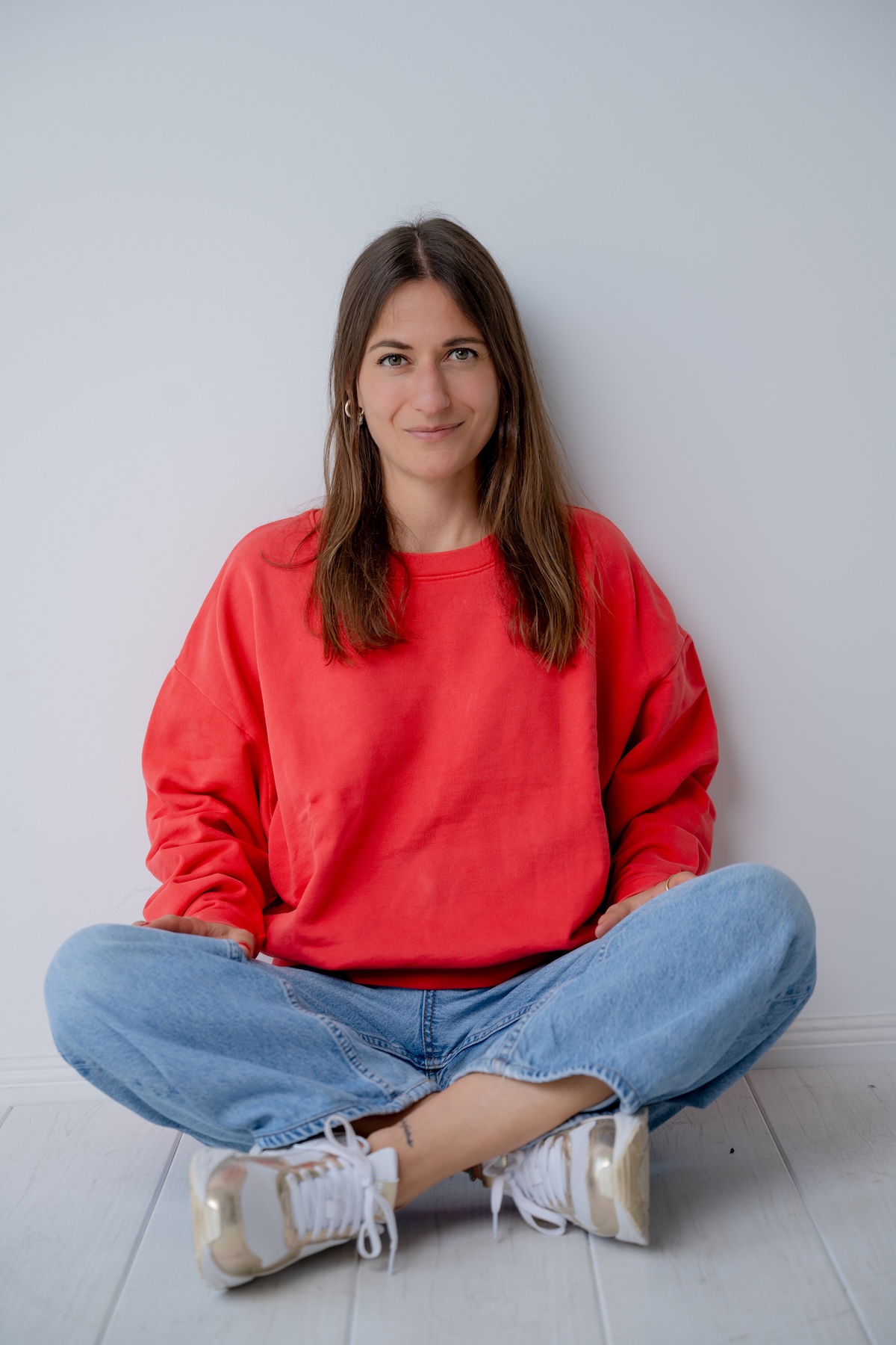 Giulia Barile, DGSv-zertifizierte systemische Supervisorin in Köln und Coach und Mentorin für Frauen in der beruflichen Neuorientierung, trägt ein rotes Shirt und eine blaue Jeans, sitzt auf dem Boden an einer Wand angelehnt