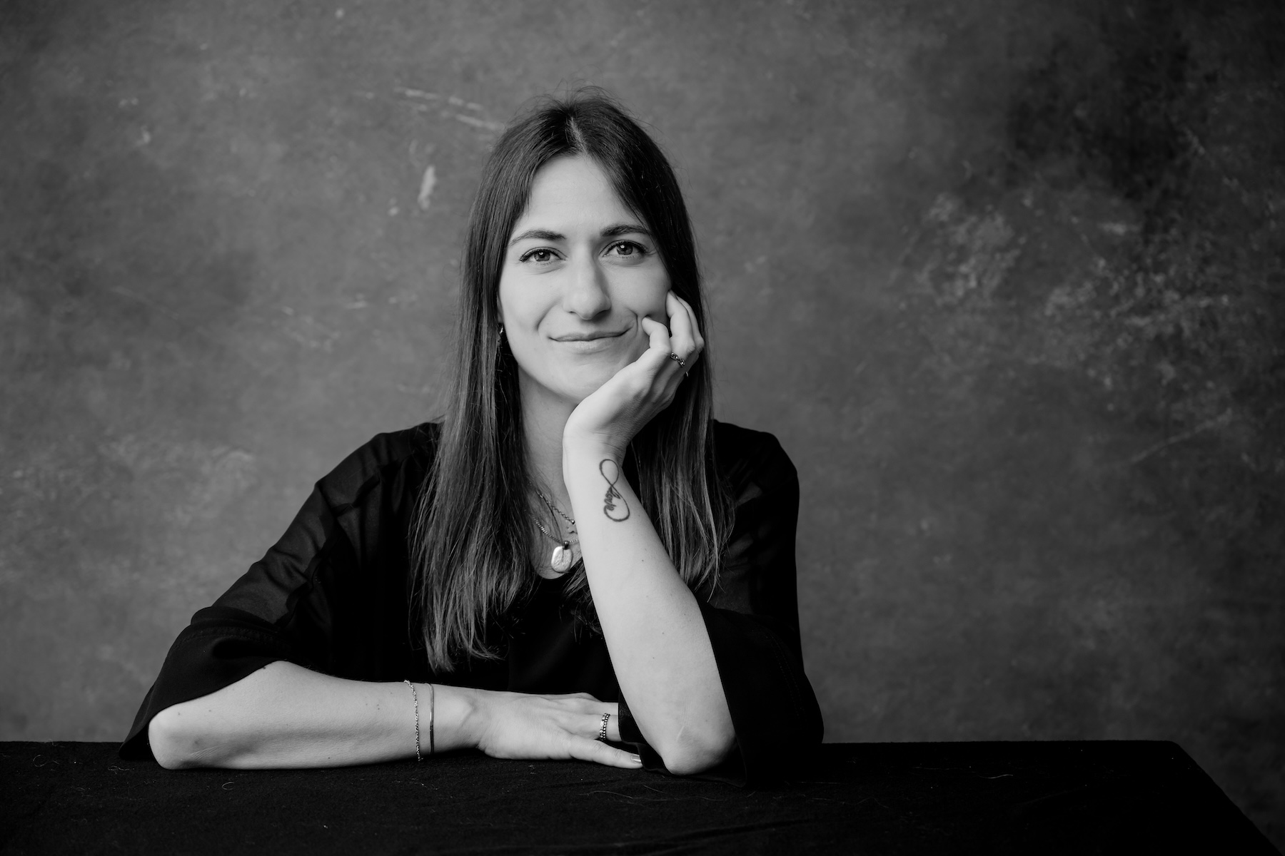 Giulia Barile, DGSv-zertifizierte systemische Supervisorin in Köln und Coach und Mentorin für Frauen in der beruflichen Neuorientierung, sitzt hinter einem Schreibtisch, den Kopf in einer Hand abgestützt und blickt direkt in die Kamera. Das Bild ist schwarz-weiß