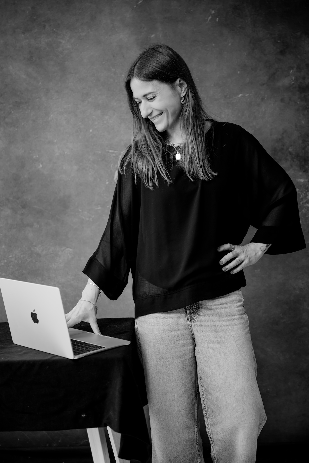 Giulia Barile, DGSv-zertifizierte systemische Supervisorin in Köln und Coach und Mentorin für Frauen in der beruflichen Neuorientierung, ist an einen Schreibtisch angelehnt und schaut auf ihrem Laptop