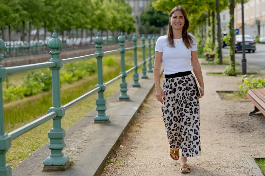 Giulia Barile, DGSv-zertifizierte systemische Supervisorin und Coach und Mentorin für Frauen in der beruflichen Neuorientierung, trägt ein weißes Shirt, einen knöchellangen Printrock, hat ihr Laptop in der linken Hand und läuft an einem Kanal entlang