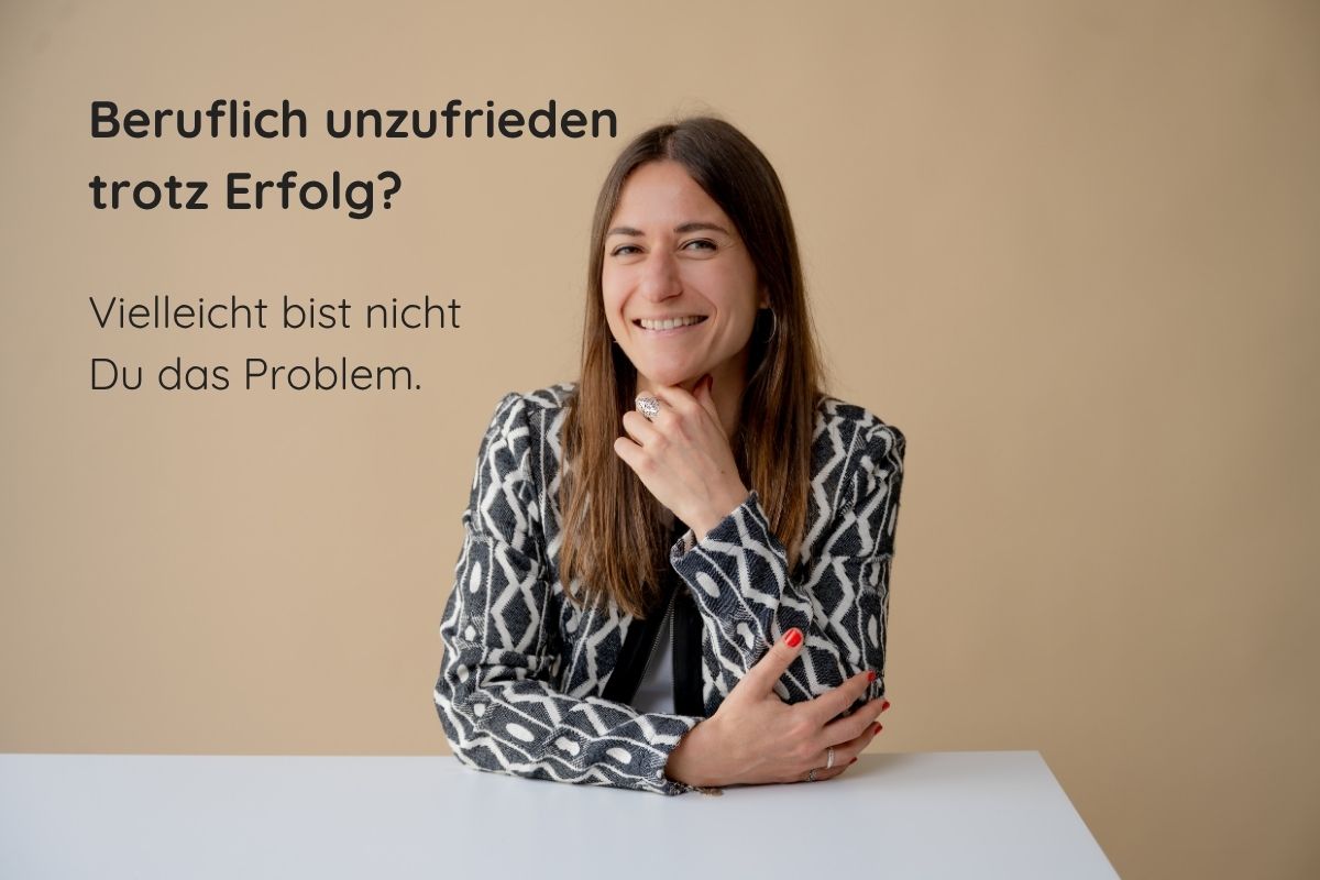 Supervisorin und Coach Giulia Barile sitzt an einem weißen Schreibtisch mit beigen Hintergrund. In der oberen linken Ecke der Schriftzug: Beruflich unzufrieden trotz Erfolg? Vielleicht bist nicht du das Problem.
